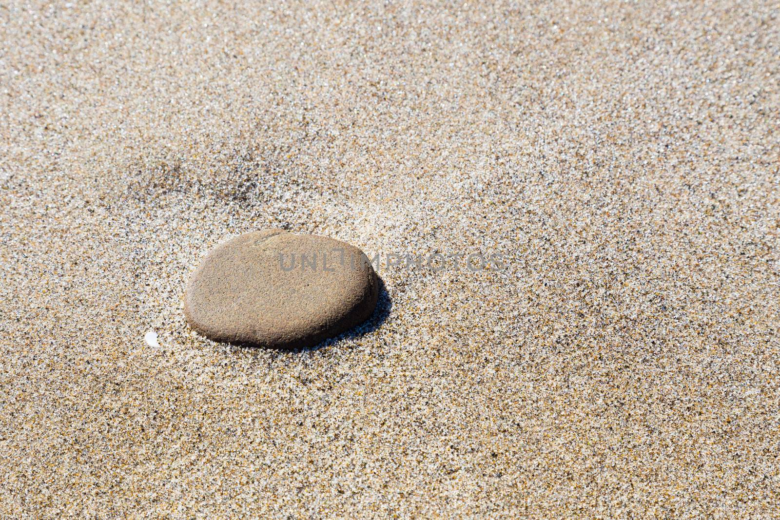 A large stone sits on some fine sand at the beach in Oregon along the coast.