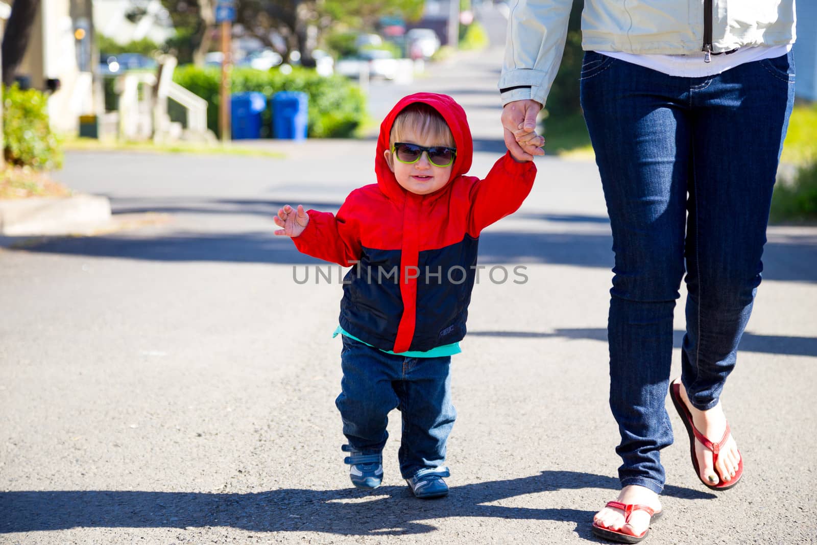 A young boy wears his sunglasses while walking back from the beach with his mom on a cool looking out of focus street.