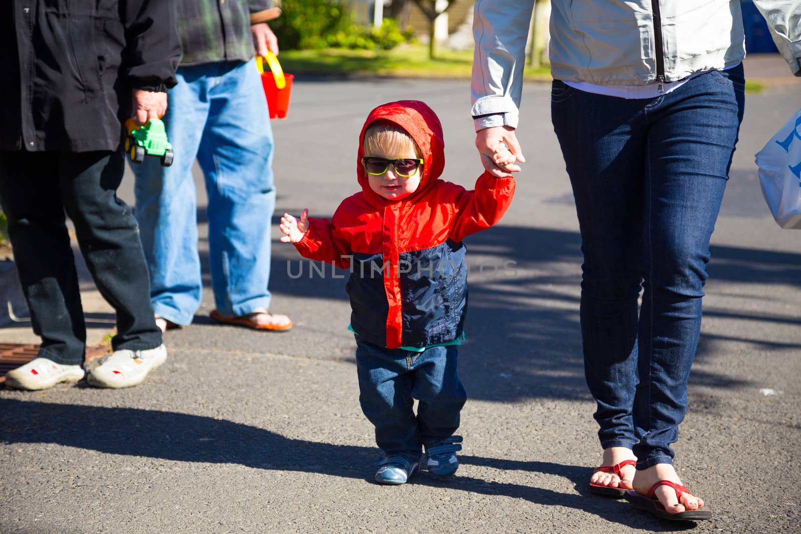 A young boy wears his sunglasses while walking back from the beach with his mom on a cool looking out of focus street.