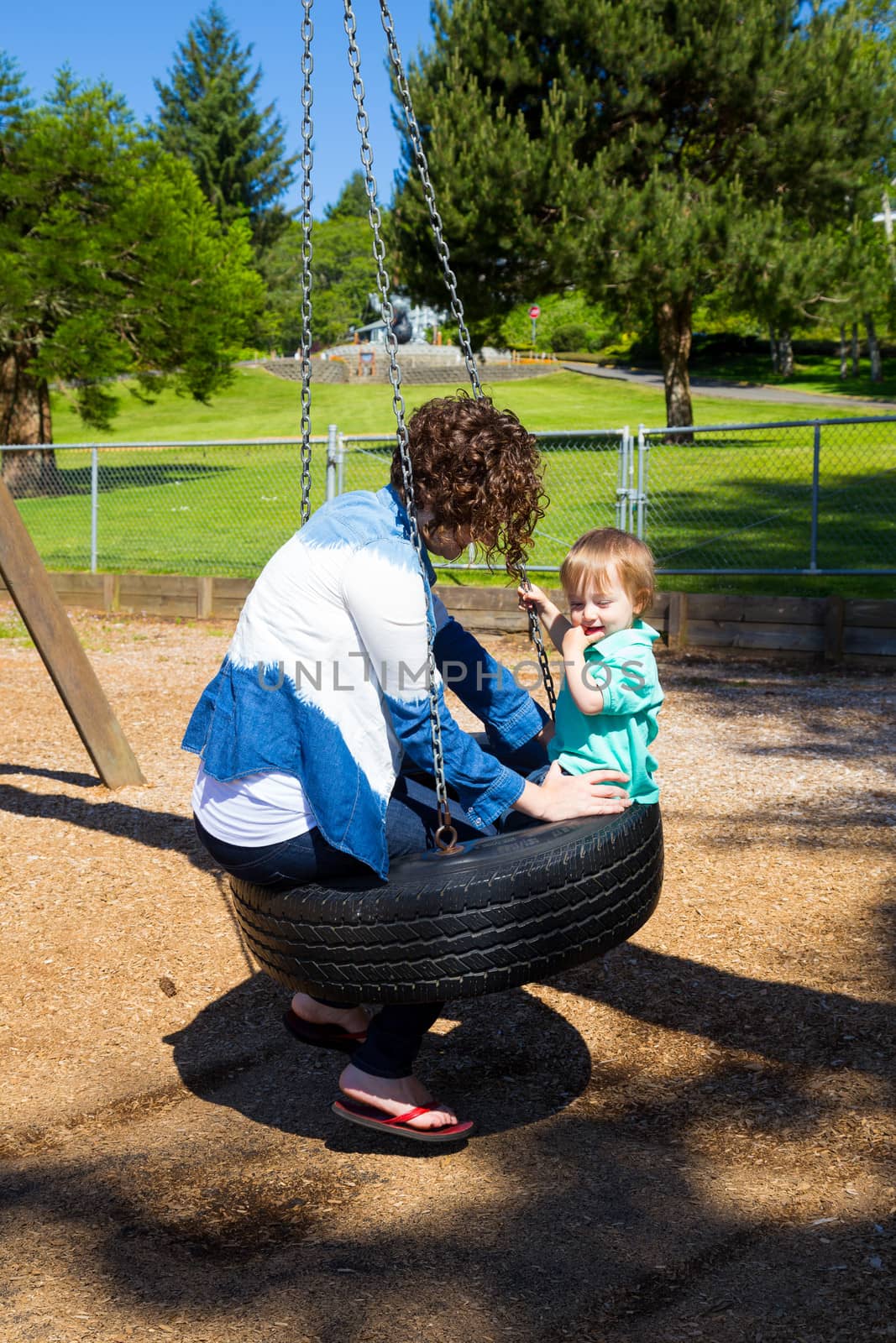 A son and his mom share a tire swing at the playground of a park in Oregon.
