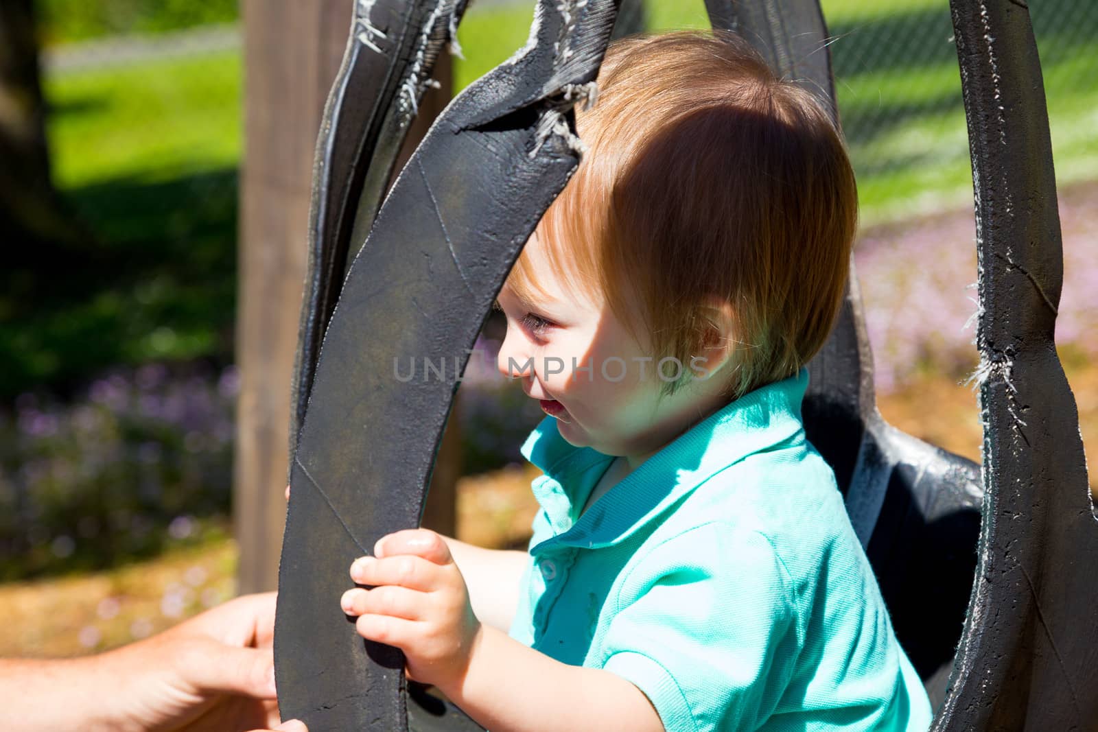 A cute young boy sits on a swing set and faces his daddy while playing at the playground in a park.