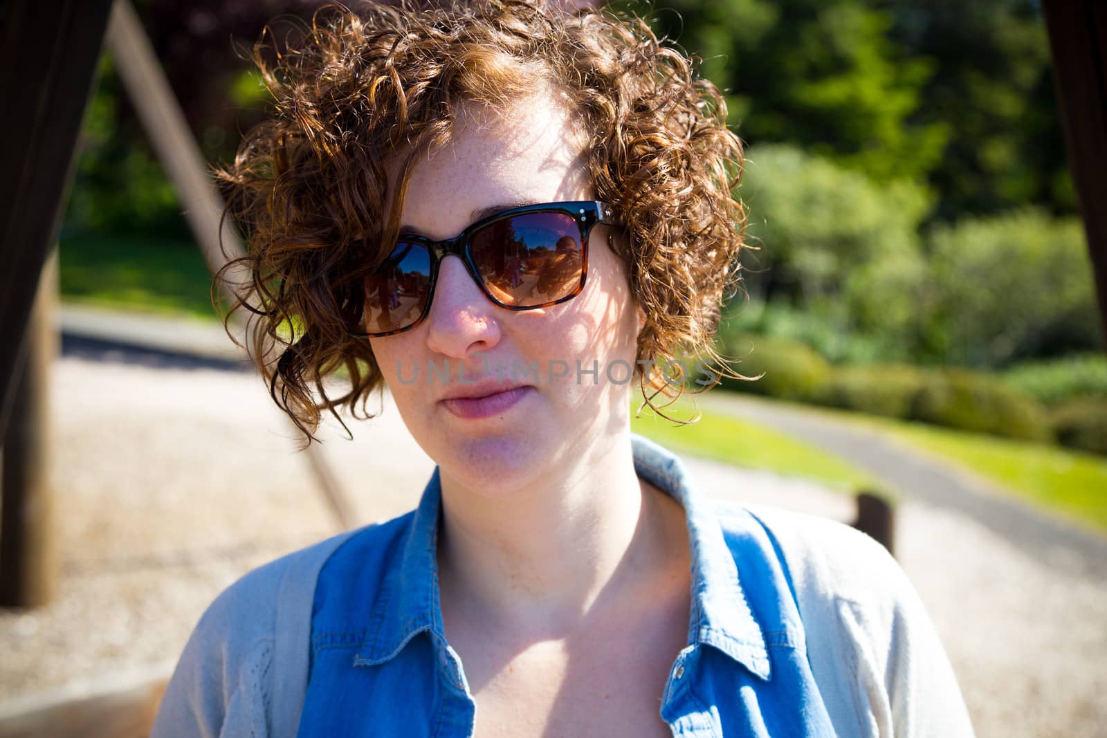 This beautiful attractive woman wears sunglasses outdoors at a park for a simple portrait of a female person.