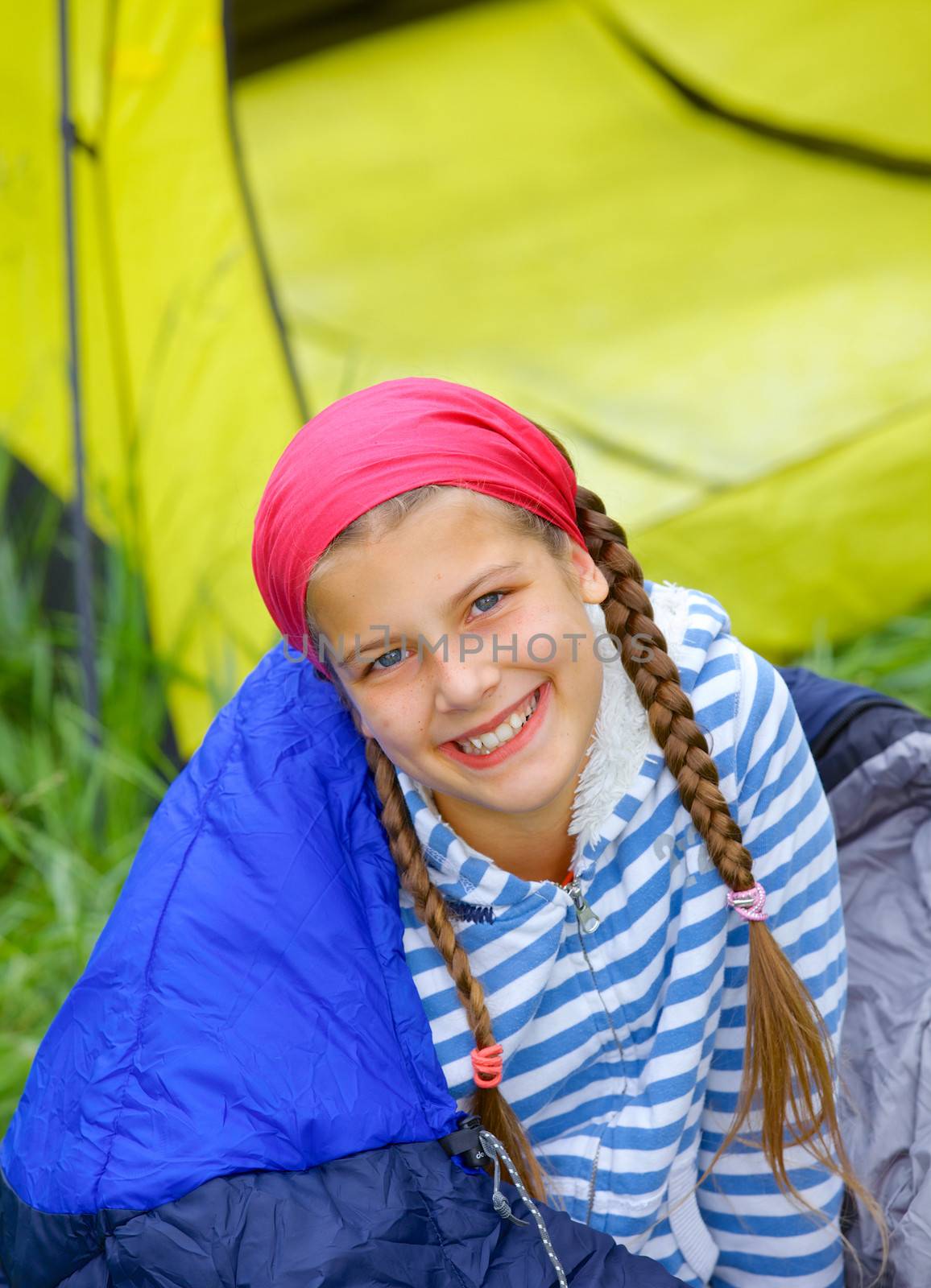 Young girl in a sleeping bag near tent in camping on the nature