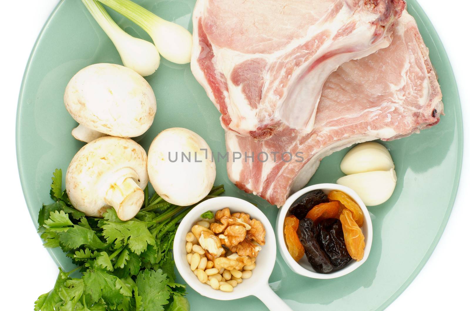Two Raw Pork Chop and Ingredients with Edible Mushrooms, Greens, Nuts, Garlic and Dried Fruits on Green Plate. Top View