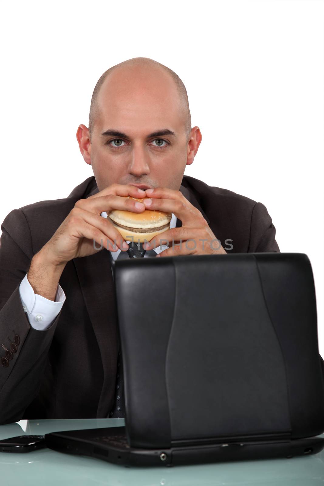 Businessman eating a burger at his desk by phovoir