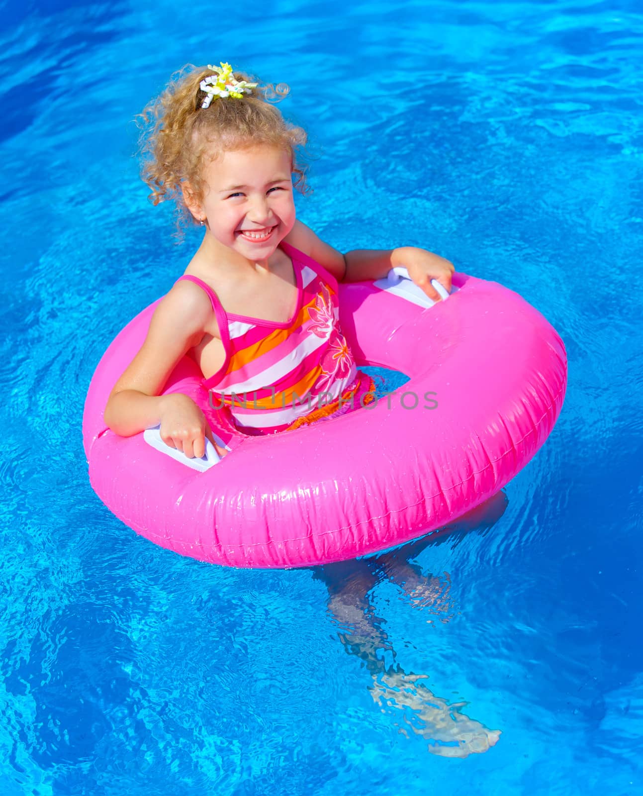 Funny little girl swims in a pool in an pink life preserver