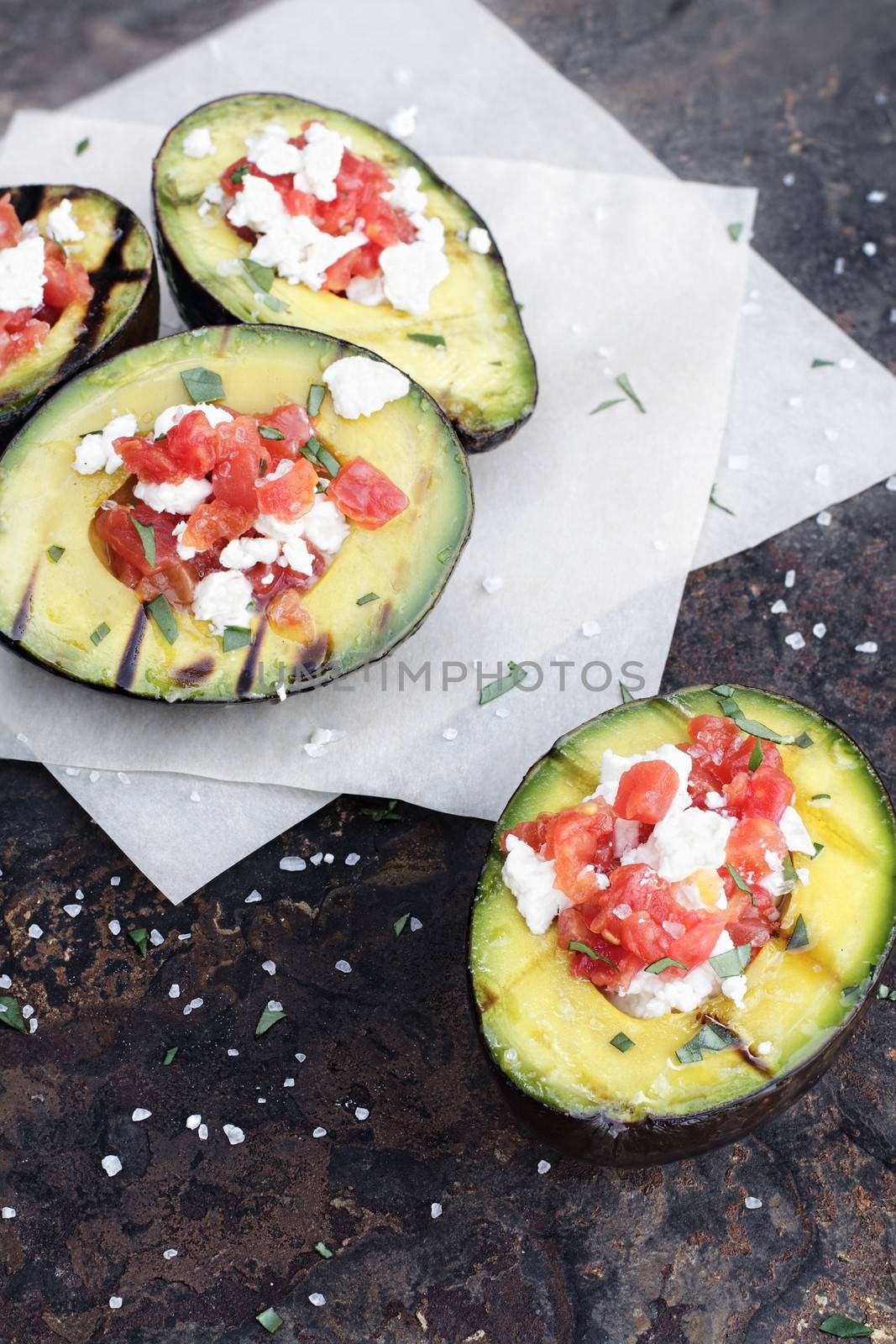 Grilled avocados filled with diced tomatoes and feta cheese and garnished with olive oil and freshly chopped parsley. 