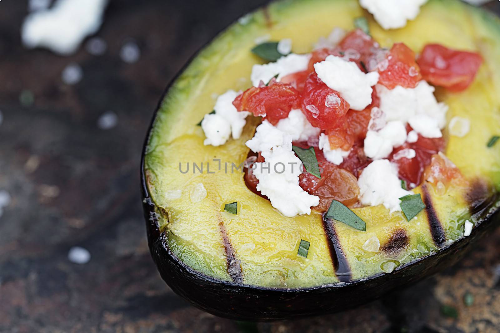Grilled avocados filled with diced tomatoes and feta cheese and garnished with olive oil and freshly chopped parsley. Extremely shallow depth of field with selective focus on the foreground.
