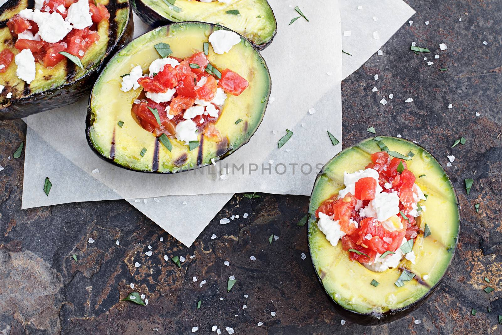 Grilled avocados filled with diced tomatoes and feta cheese and garnished with olive oil and freshly chopped parsley. 