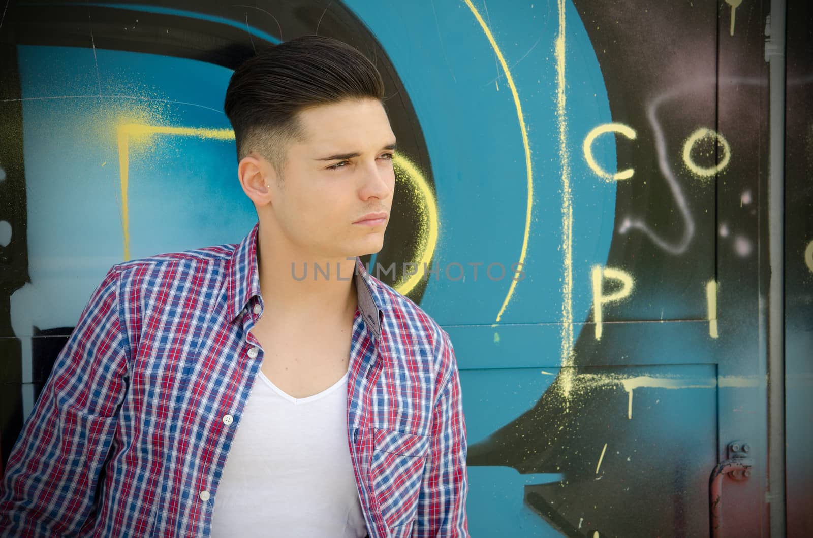 Handsome young man against colorful graffiti covered wall