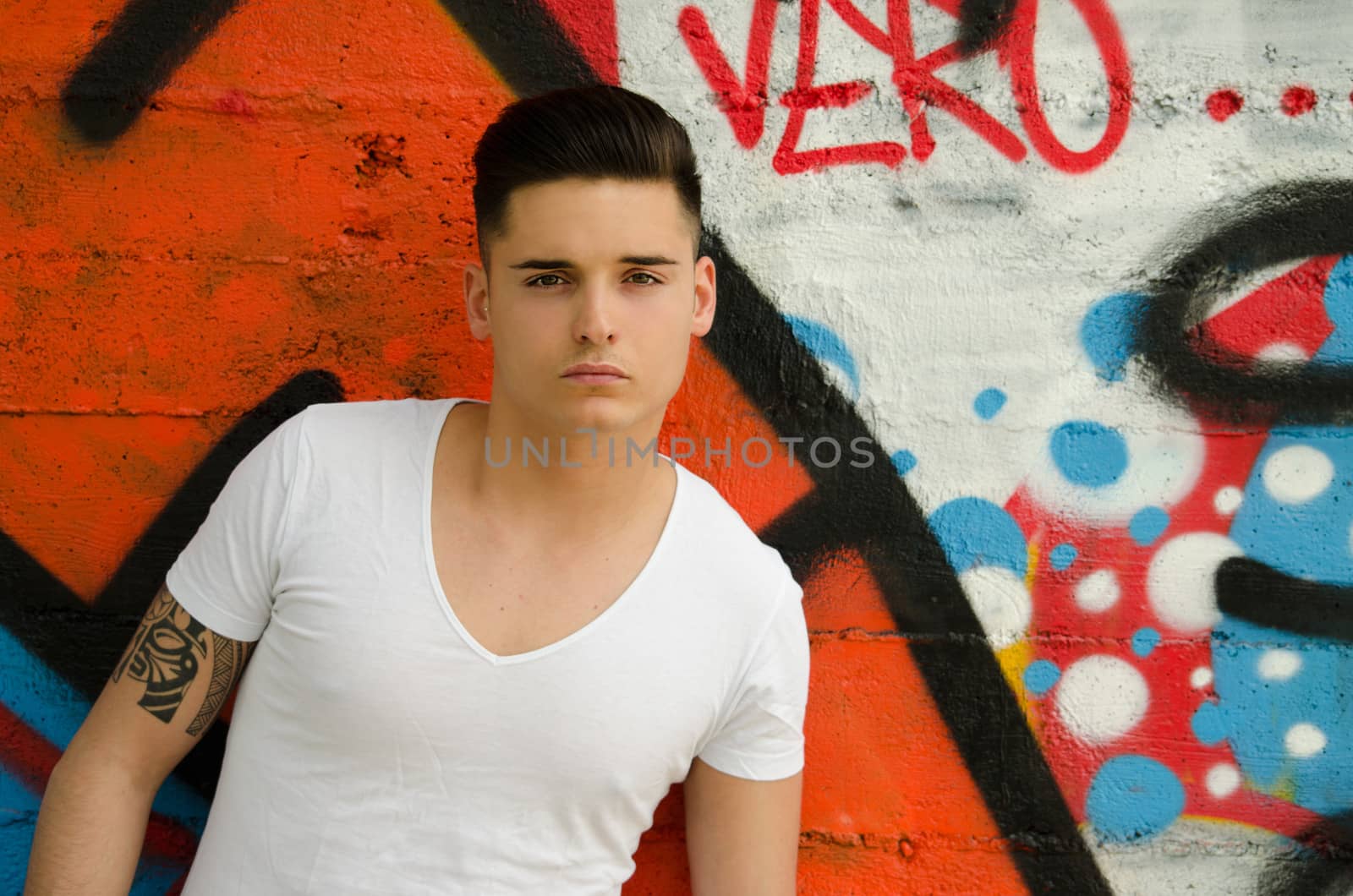 Handsome young man against colorful graffiti covered wall