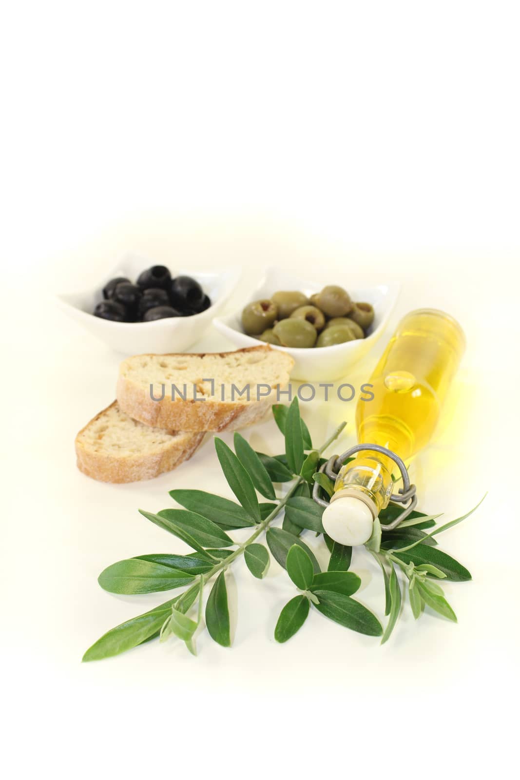 Bottle of olive oil with fresh olives, baguette and olive branch on a bright background