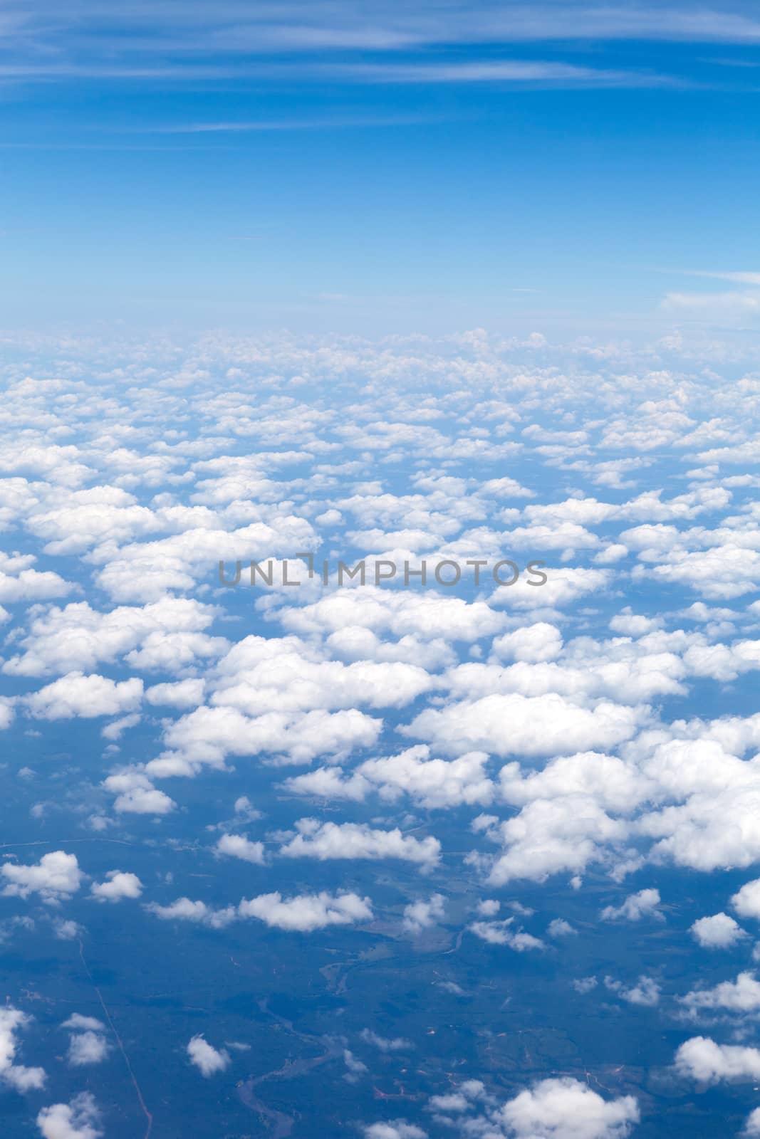 Aerial view of the blue skies and horizon with fluffy clouds and the earth below.
