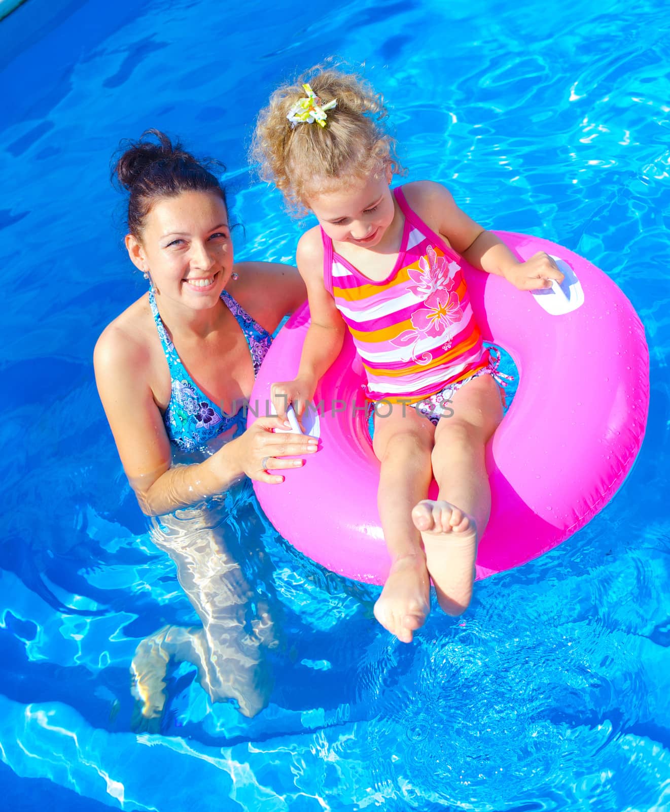 Pretty little girl with her mother in swimming pool outdoors. Vertical view