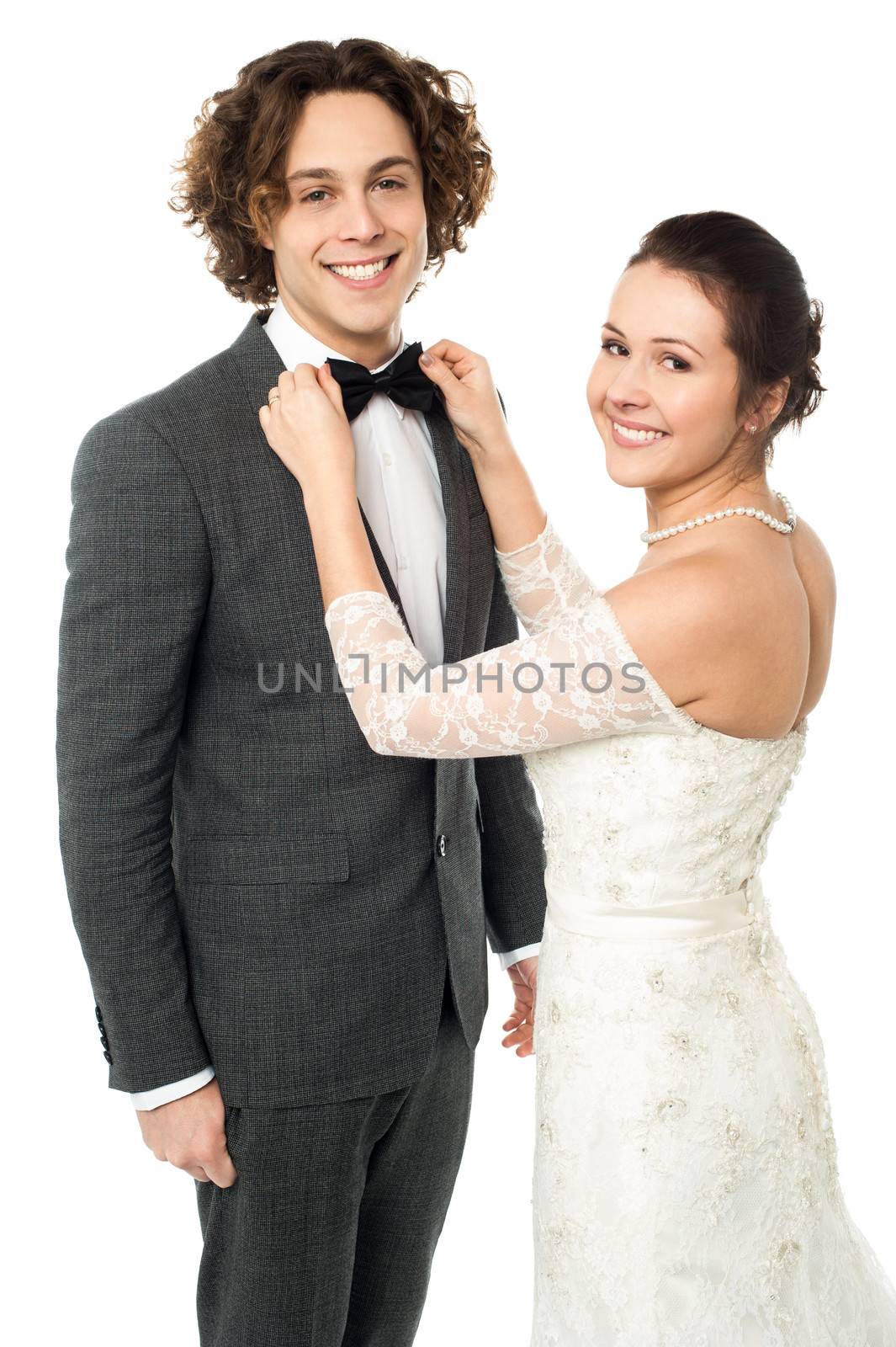 Glamorous young smiling bride adjusting the bowtie of a groom.