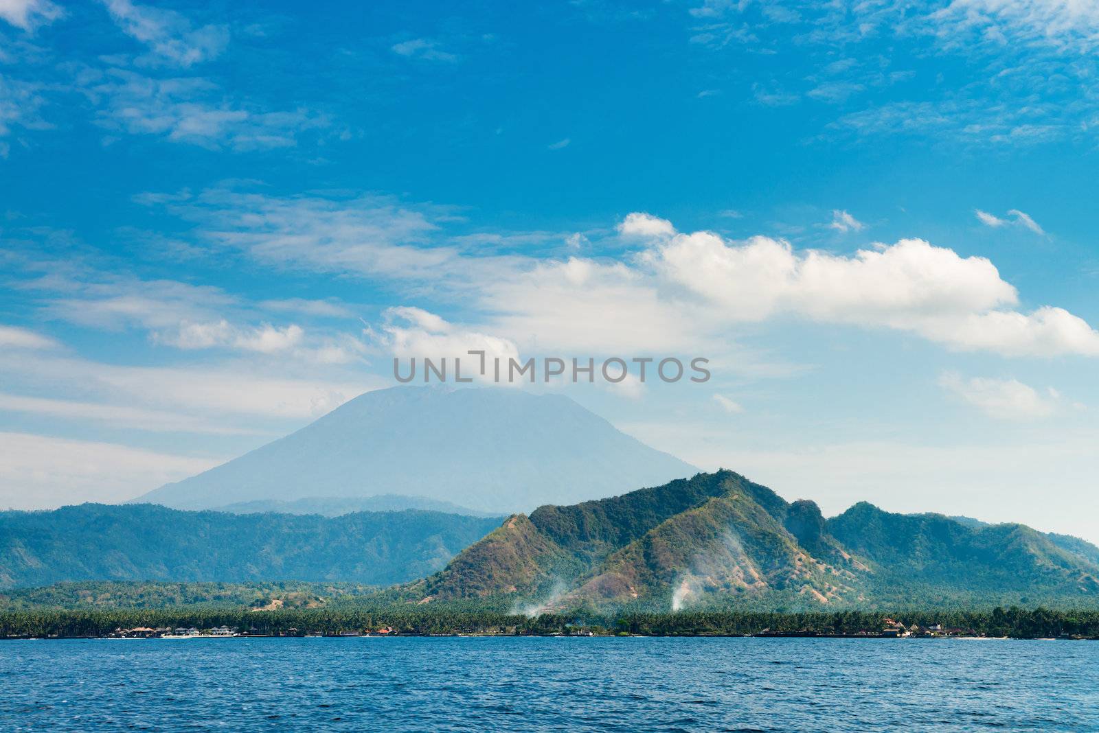 Gunung Agung the highest volcano on Bali island, Indonesia with blue cloudy sky and sea on front.