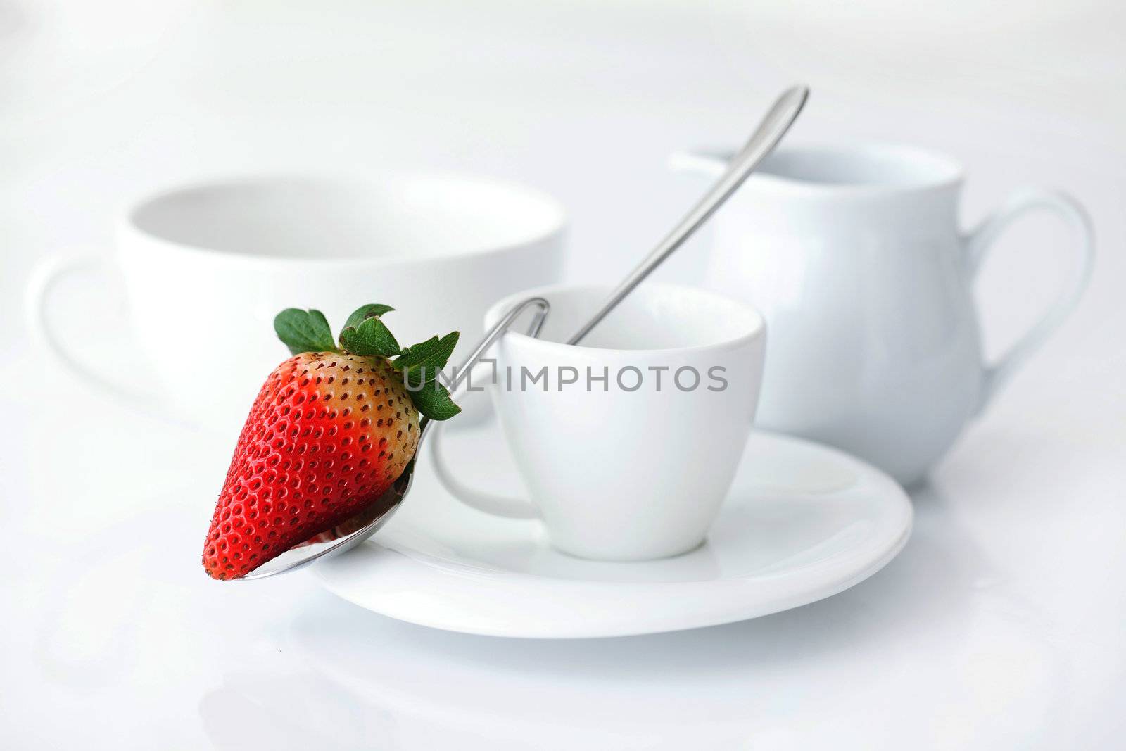 white cup with saucer, milk jug and strawberry