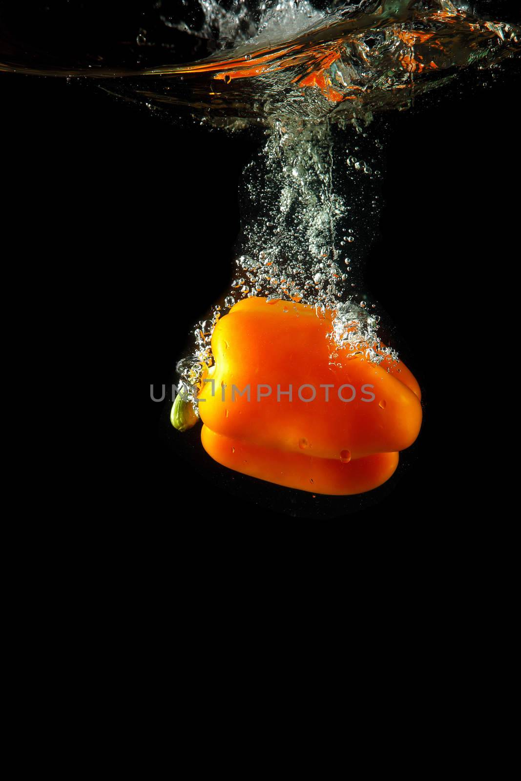 Colored orange paprika in water splashes on black background