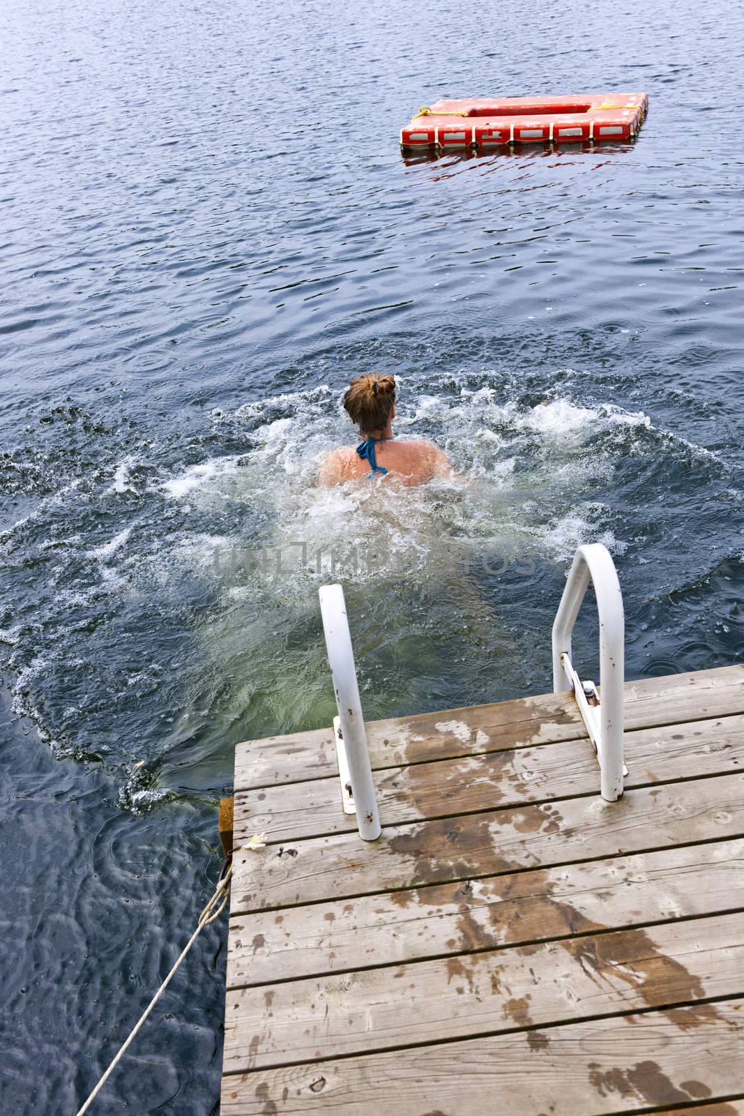 Teen girl splashing and swimming in lake near dock