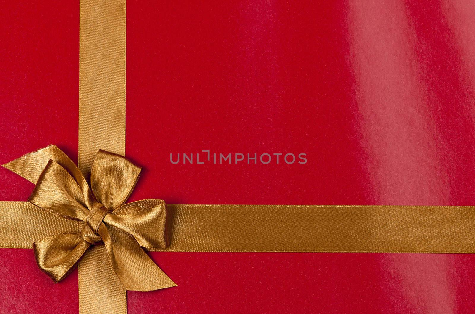 Red background of present wrapped with gold satin ribbon and bow