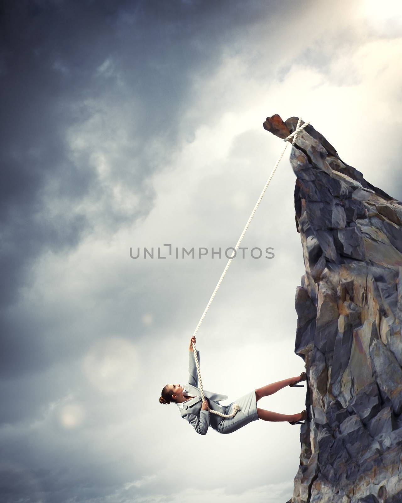 businesswoman climbing steep mountain hanging on rope