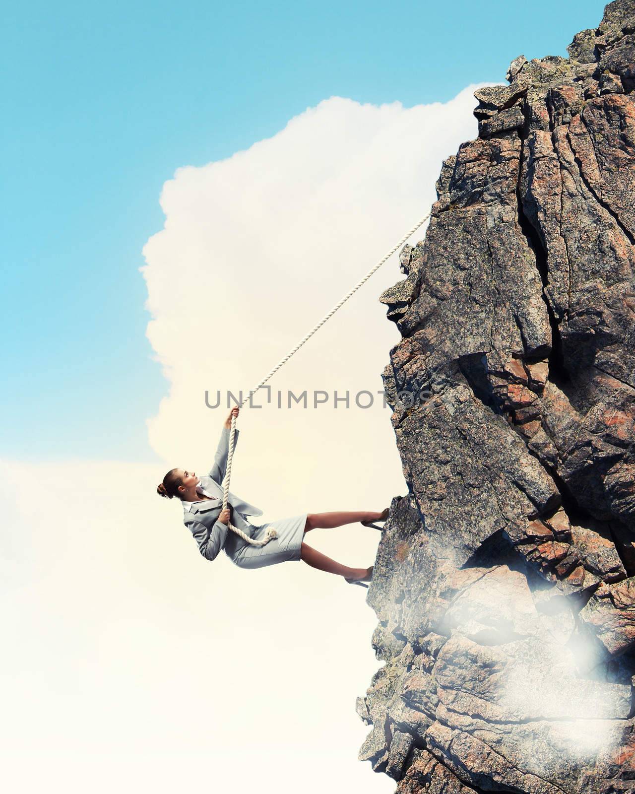 businesswoman climbing steep mountain hanging on rope