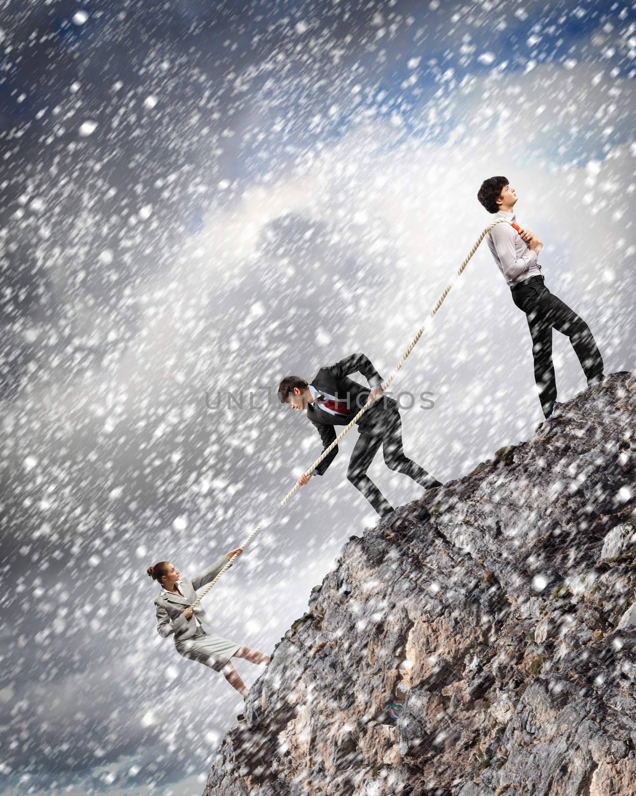 Image of three businesspeople pulling rope atop mountain