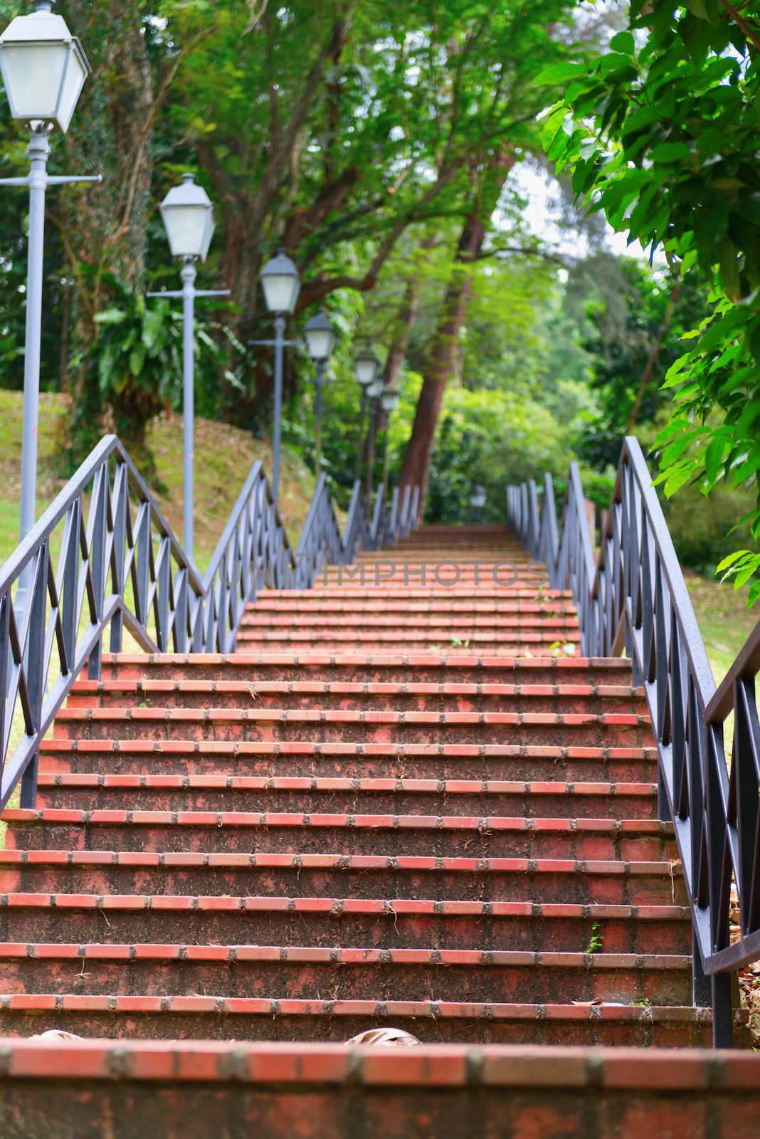 Red stone stairs on in a park with handrail and street lamp