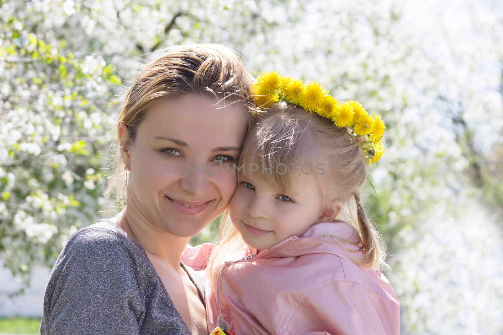 Happy mothre and baby girl in spring garden with dandelion wreath