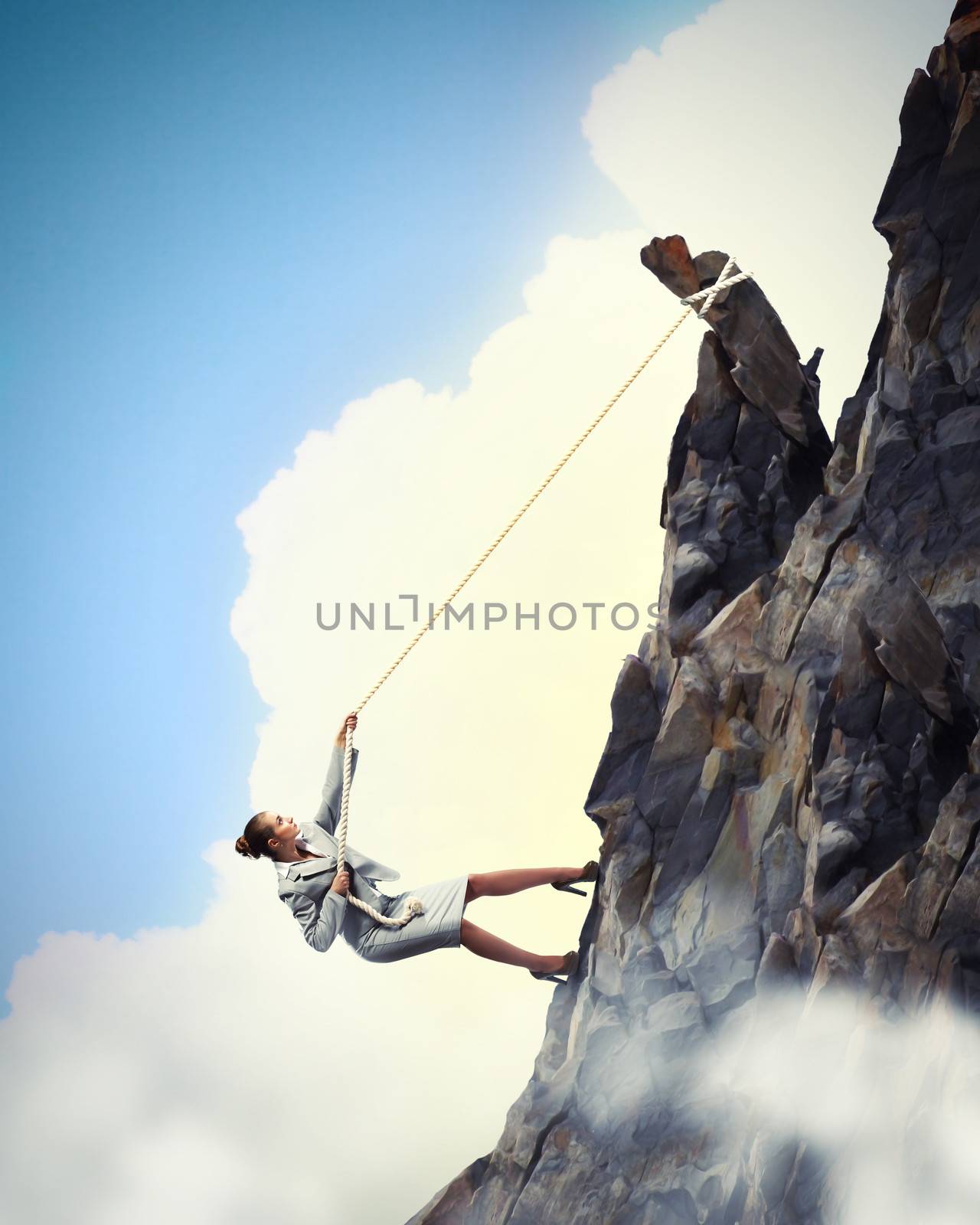 businesswoman climbing steep mountain hanging on rope