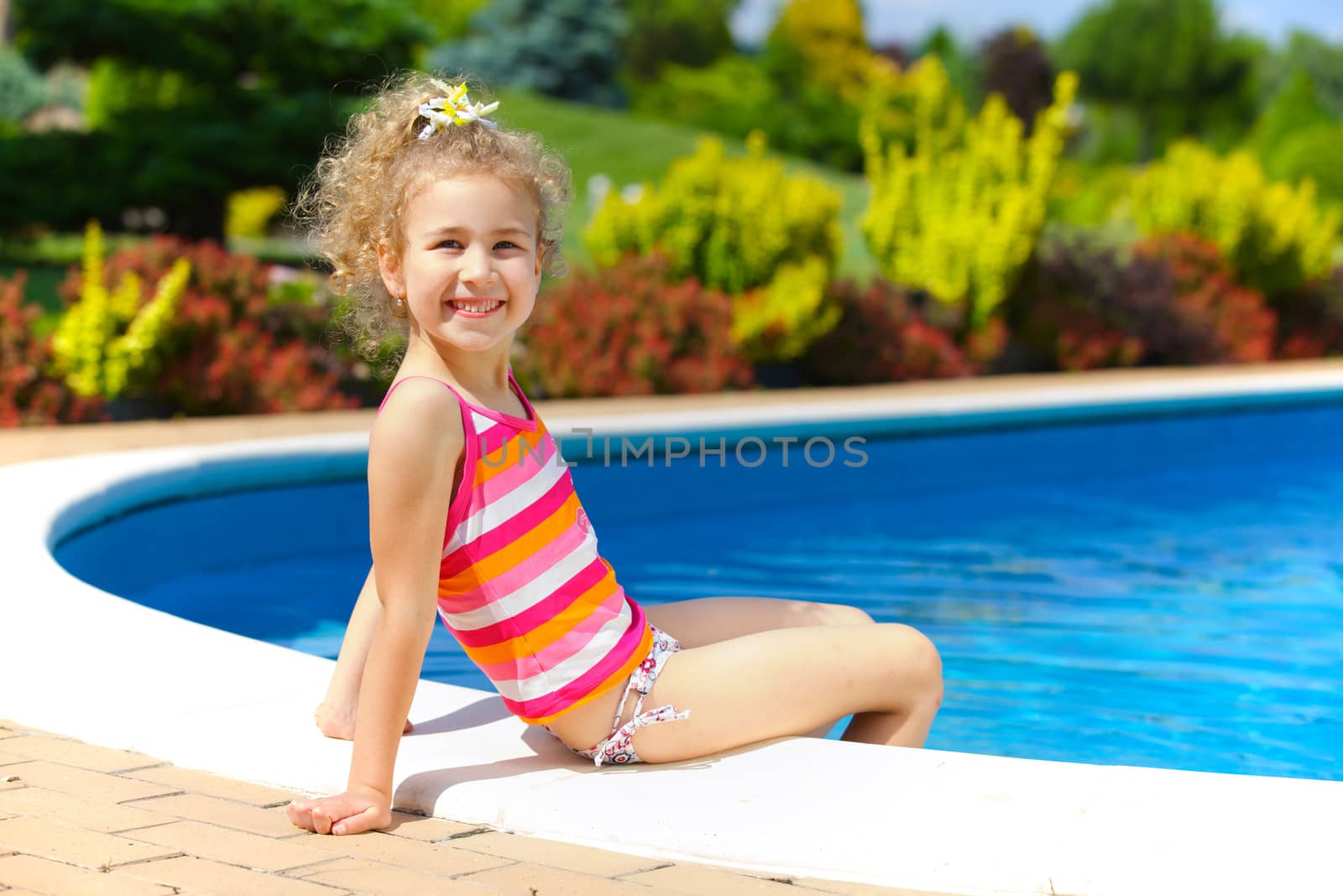 Pretty little girl sitting near swimming pool
