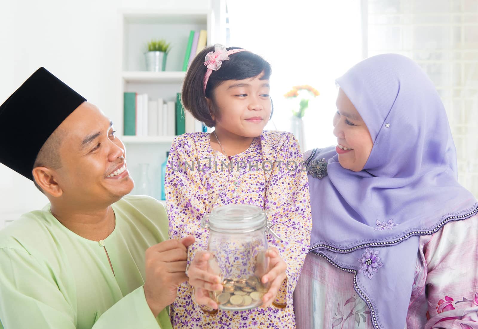 Islamic banking concept. Southeast Asian Malay family saving money at home. Muslim father, mother and daughter living lifestyle.