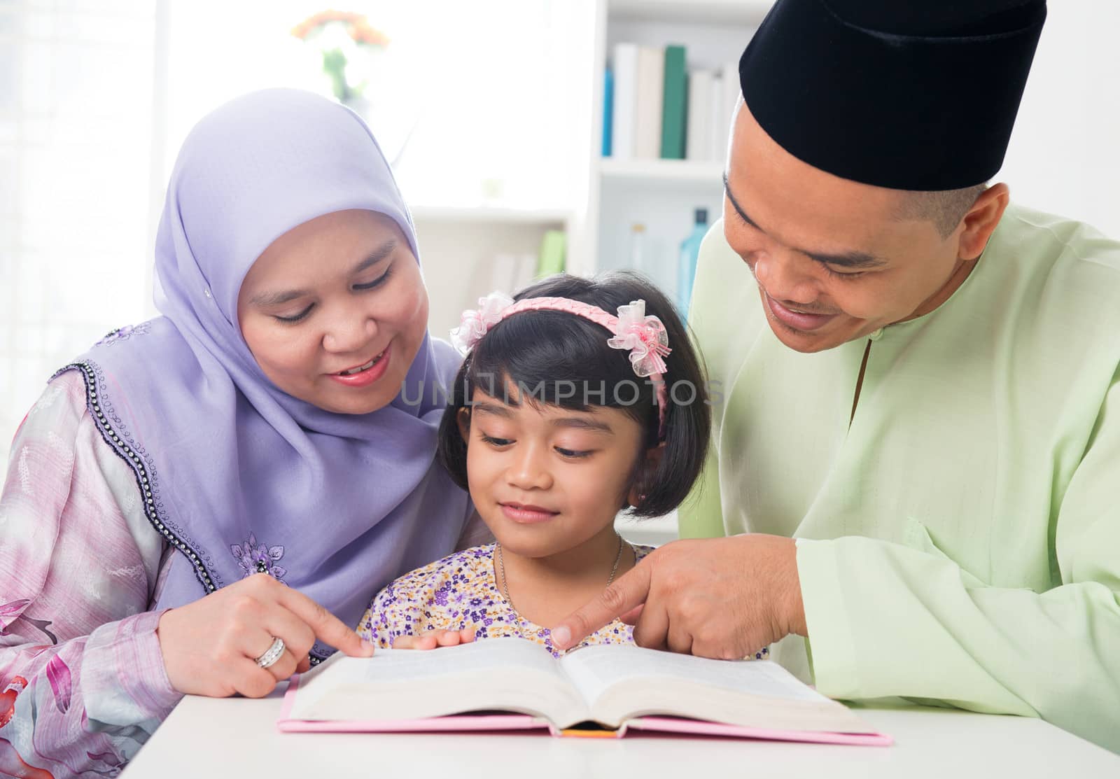 Malay Muslim parents teaching child reading a book. Southeast Asian family at home. 
