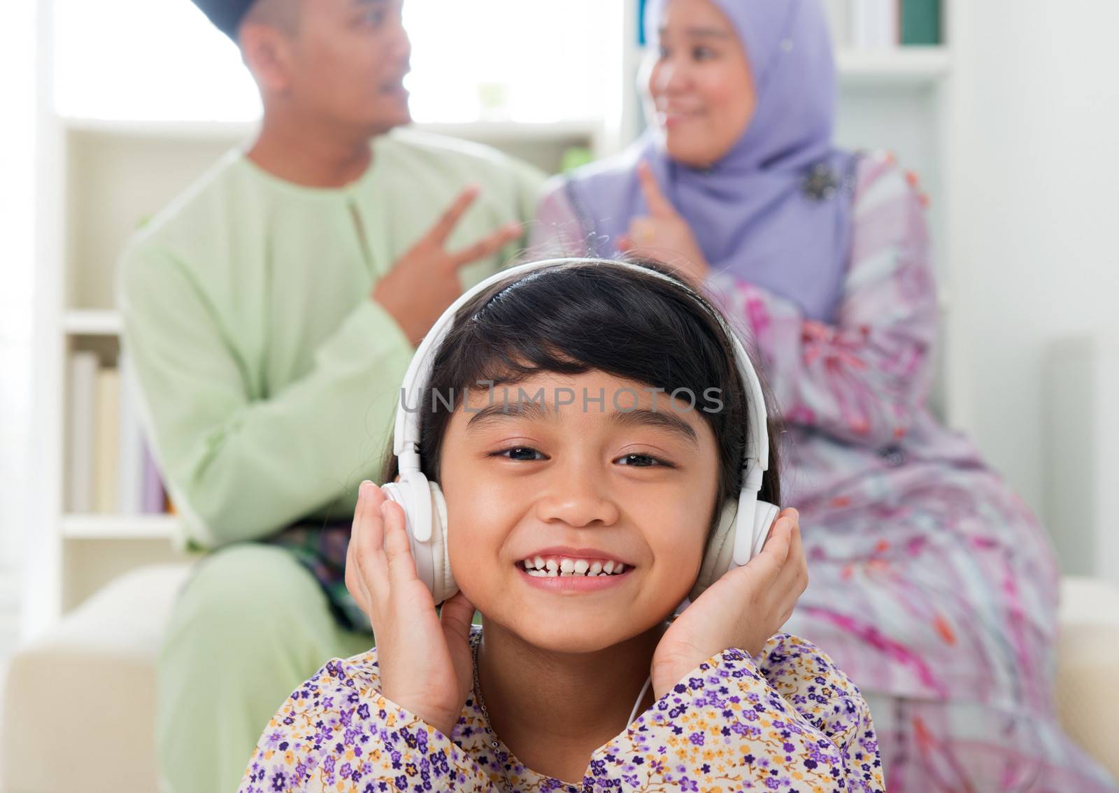 Muslim girl listening to song at home. Southeast Asian family living lifestyle. Happy smiling Malay parents and child.