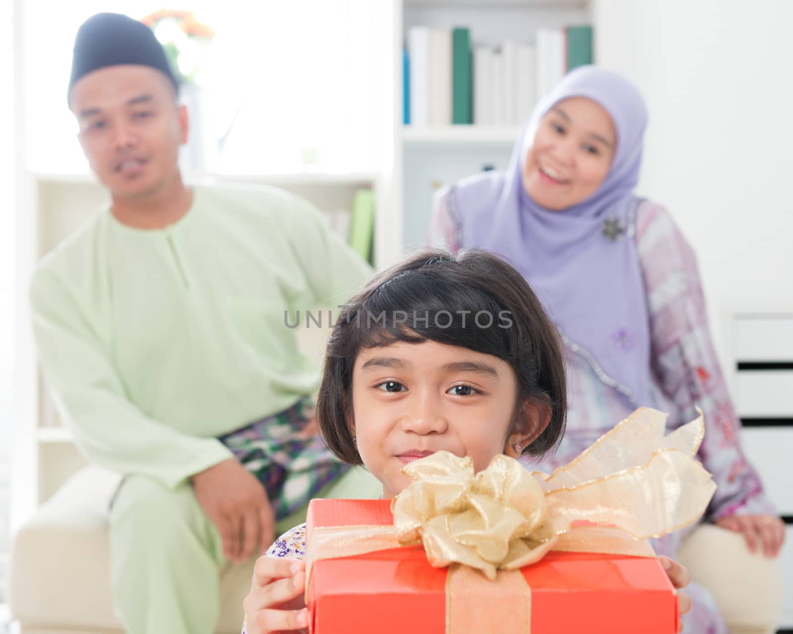 Southeast Asian girl with gift box. Muslim family living lifestyle. Happy smiling Malay parents and child.