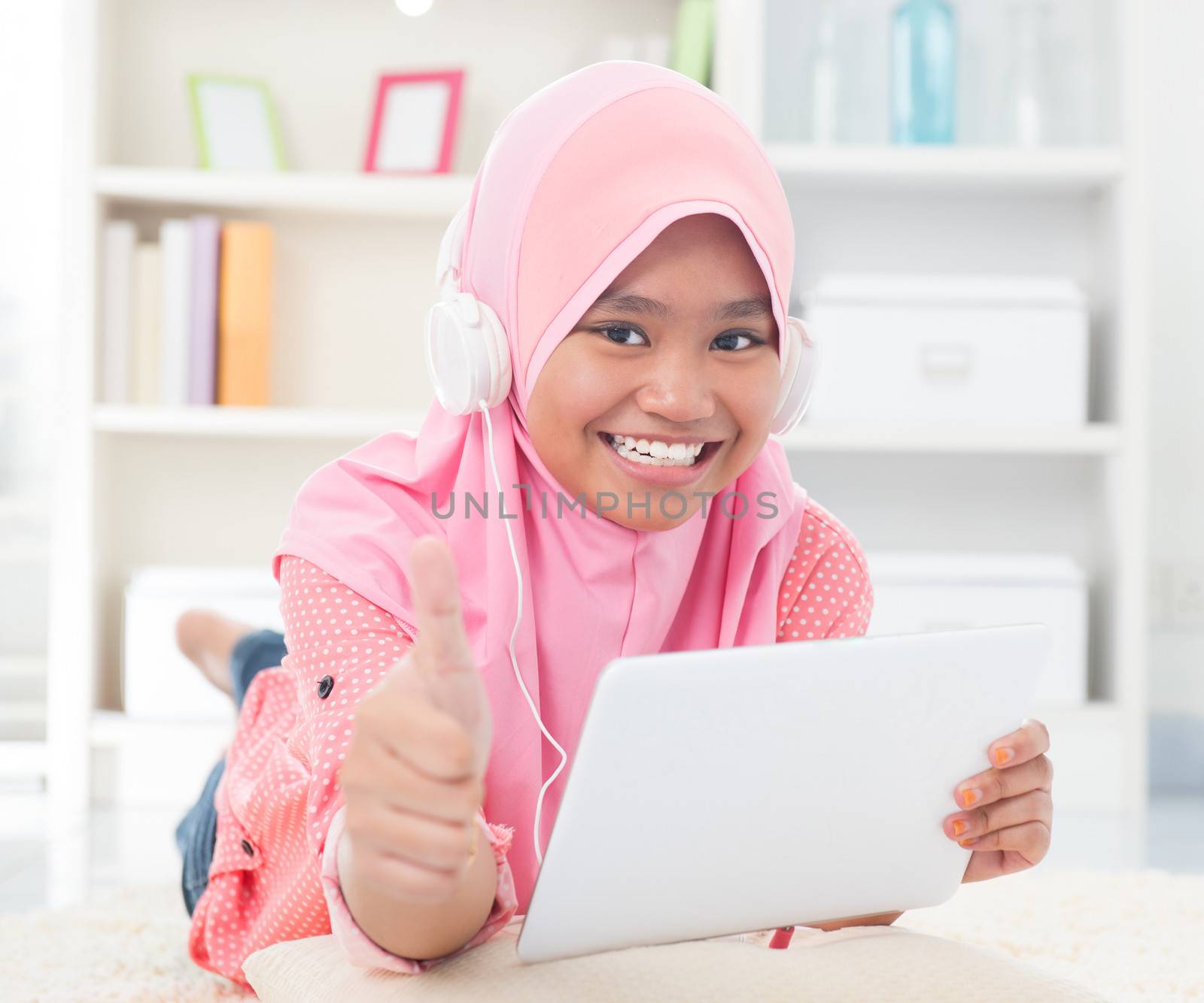 Asian teen listening to music with headphone and thumb up. Southeast Asian teenager at home. Muslim teenage girl living lifestyle.