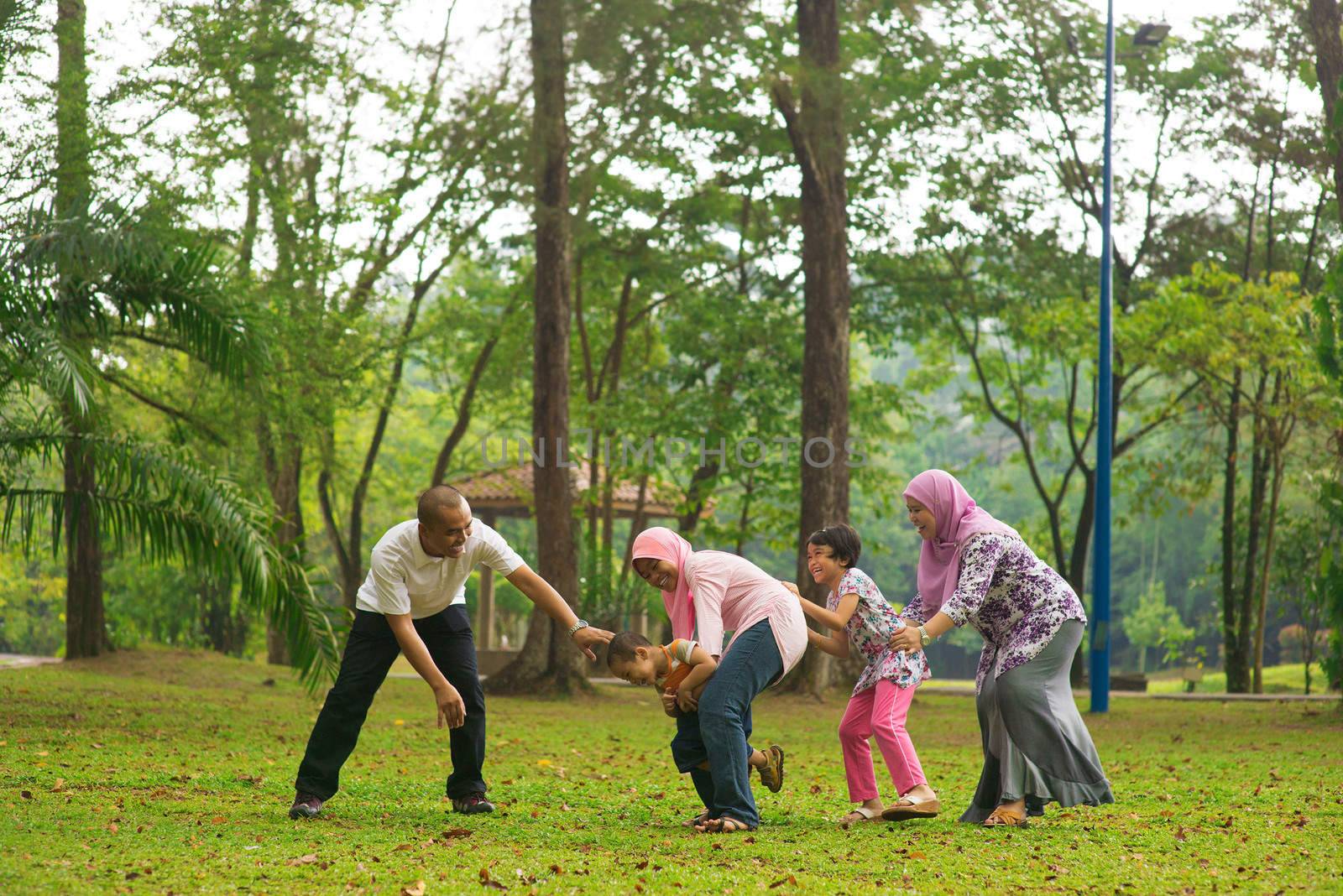 Muslim family having fun at green outdoor park. Beautiful Southeast Asian family playing together.