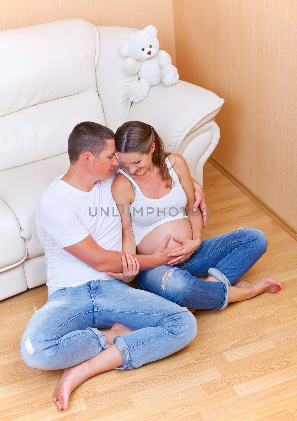 Couple sitting near a sofa and smiling and pending the kid