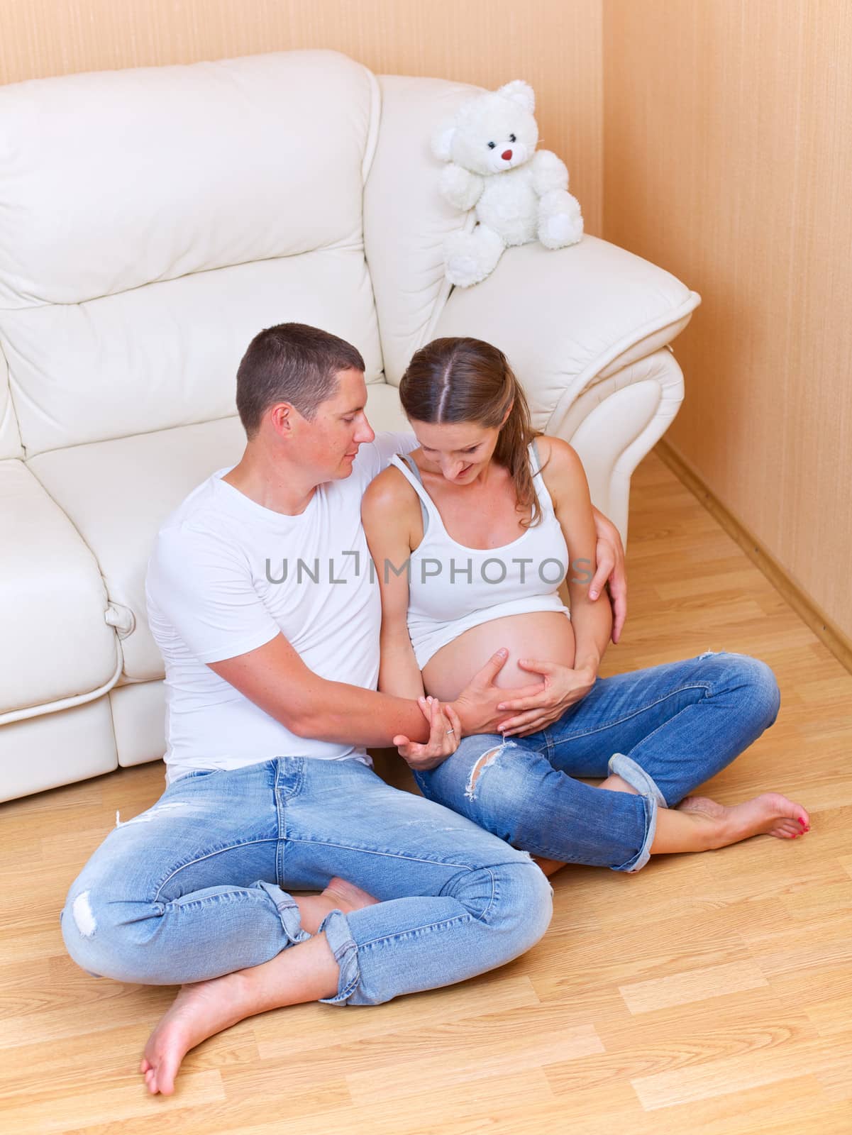 Couple sitting near a sofa and smiling and pending the kid