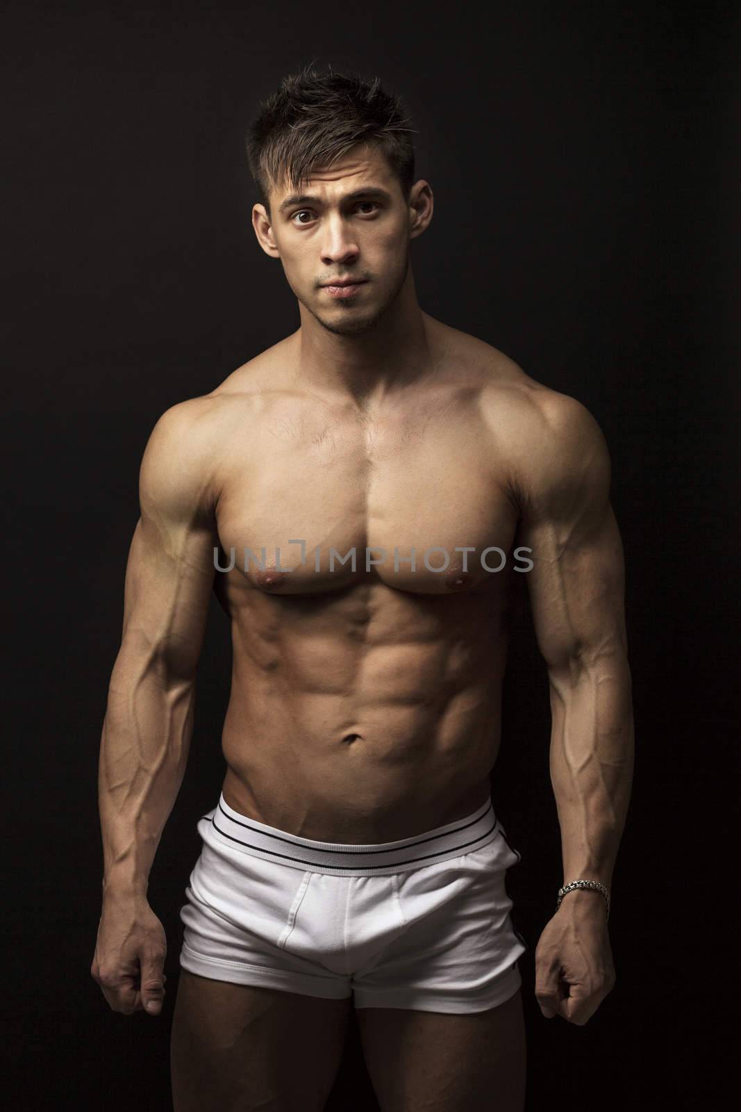 Portrait of muscular young man over black background