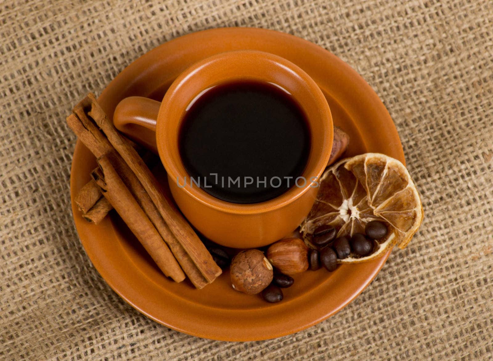 Closeup shot of freshly prepared cup of italian espresso with cinnamon, coffe beans, nuts and lemon over sacking