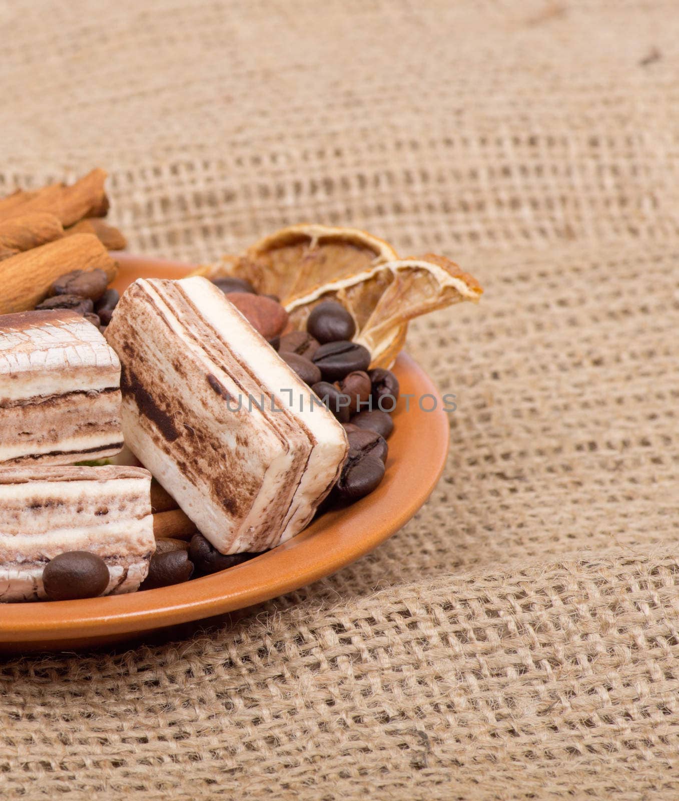 Sweets, cinnamon, nuts and coffee beans on a saucer, on burlap background.