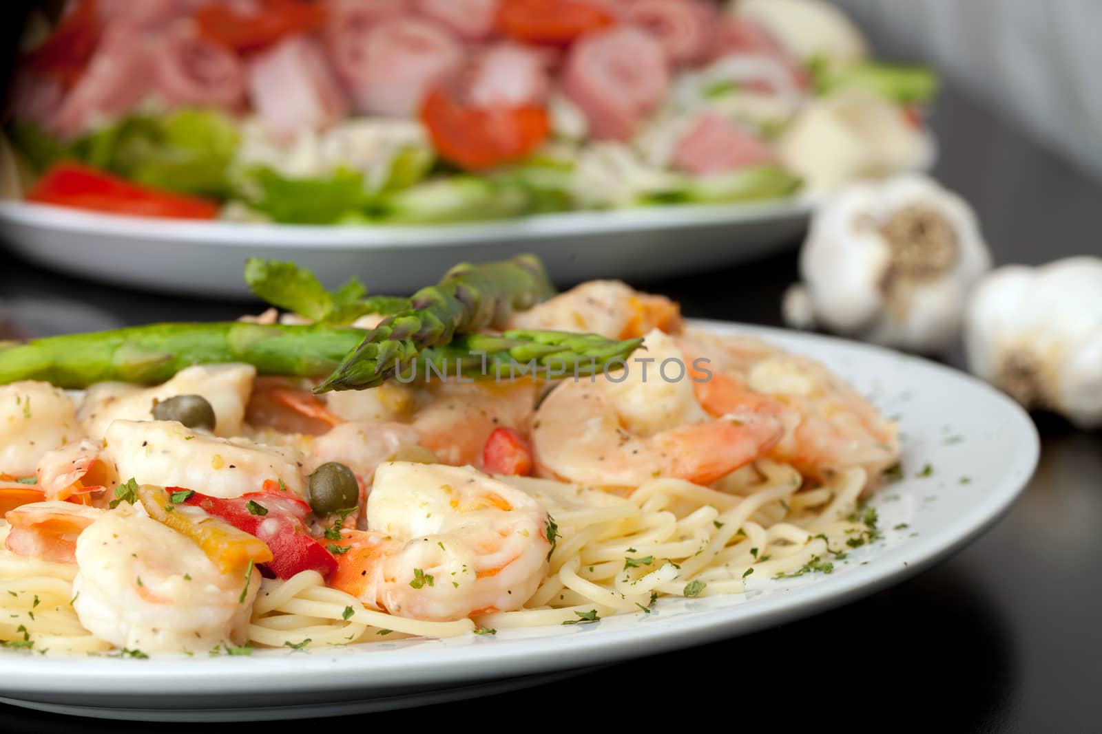 A delicious shrimp scampi pasta dish with antipasto salad in the background.