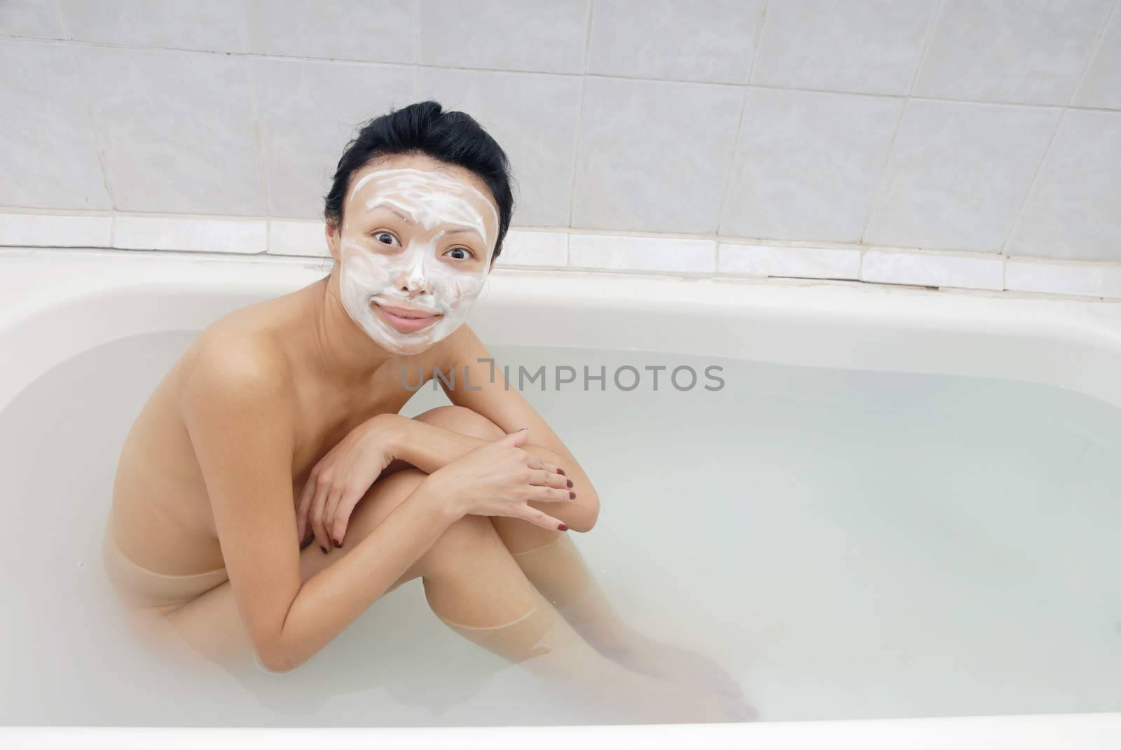 Smiling model with beauty mask sitting in the bath