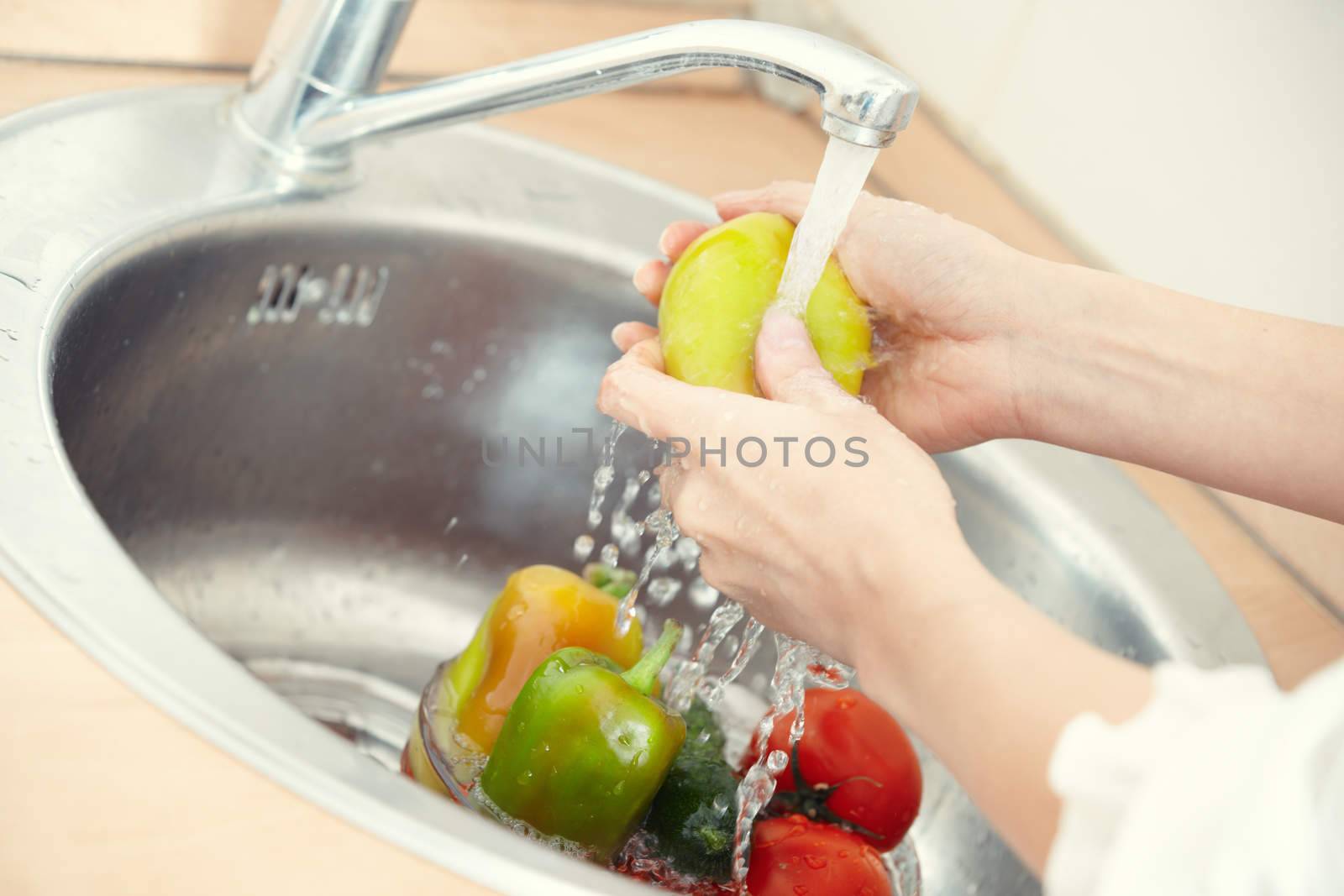 Hands of woman washing vegetables at her kitchen