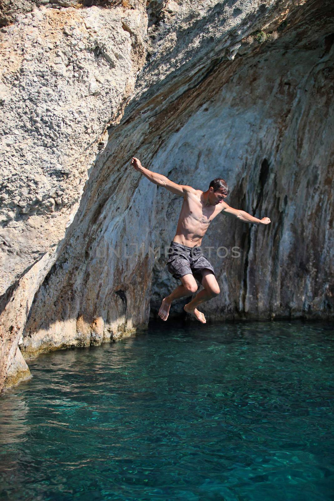Young man jumping from cliff into sea