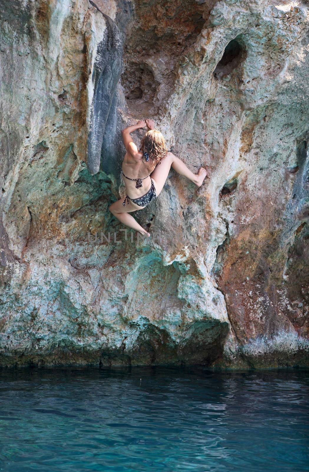Deep water soloing, young female rock climber on face of cliff
