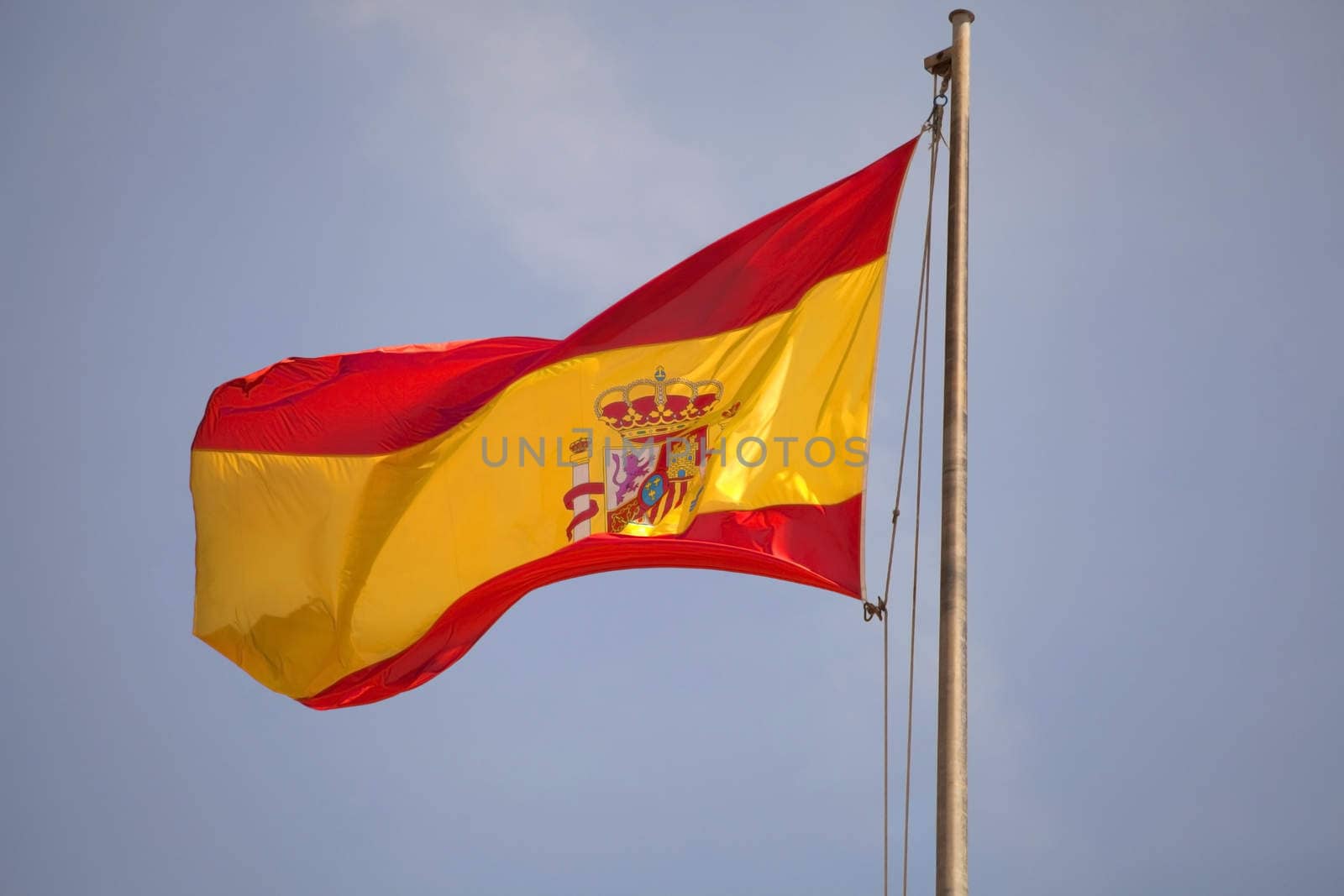 Spanish flag waving in blue sky.