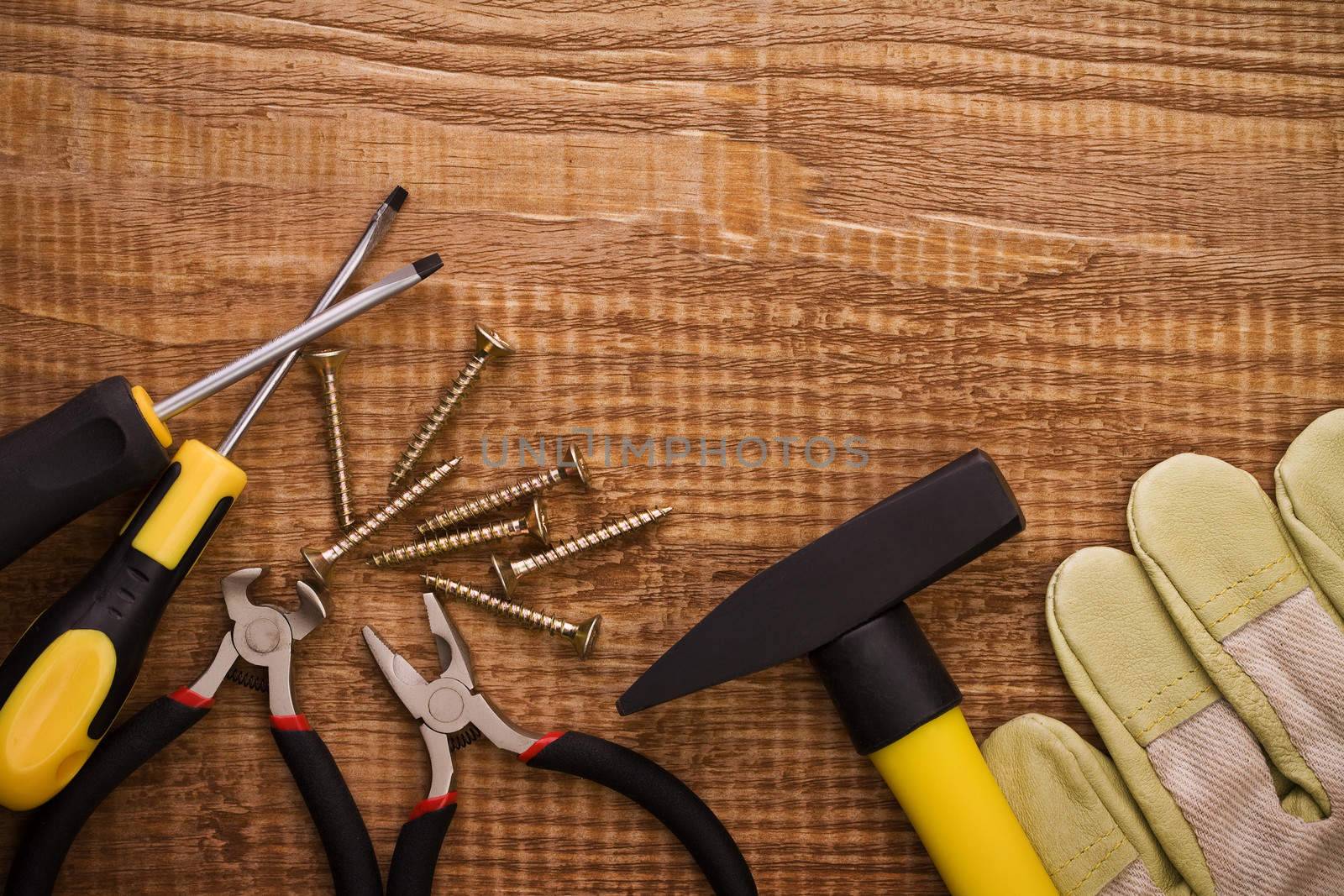 hamer pliers screwdriwer and gloves on woodn board