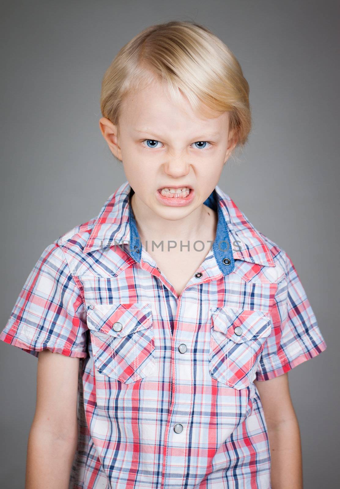 A frustrated and angry looking young boy  pulling a face. Isolated on white.